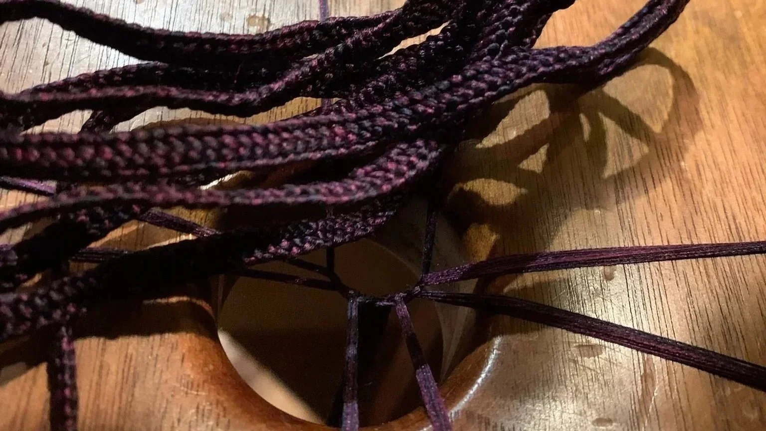 Purple and blue braided rope sit atop a wooden weaving fixture.