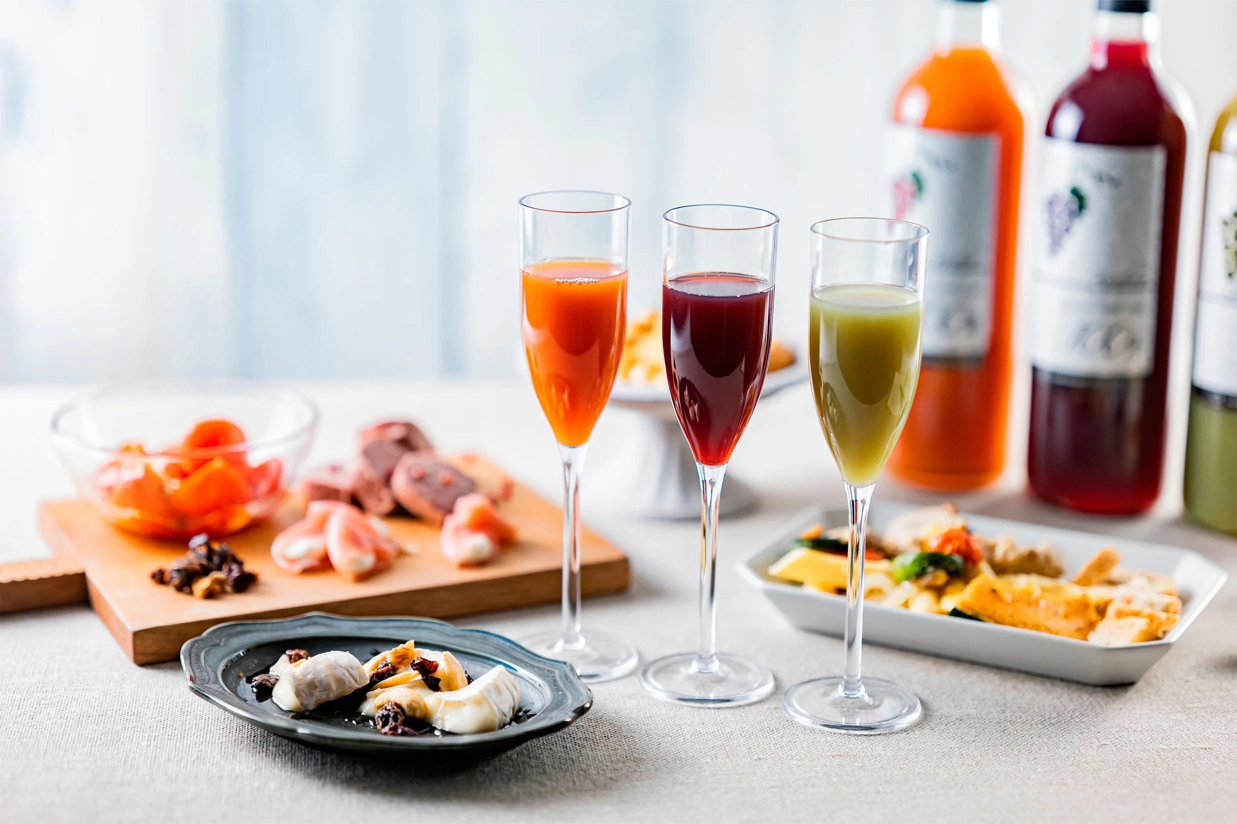 Three flutes of wine with appetizer-sized food around the the flutes and the three bottles of win in the background.