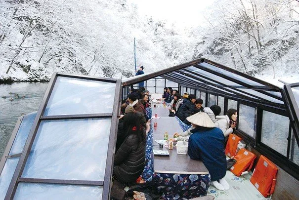 River boat cruise in the winter with glass covering and traditional Japanese table and blanket to keep warm in Geibiki Gorge in Aomori, Japan.