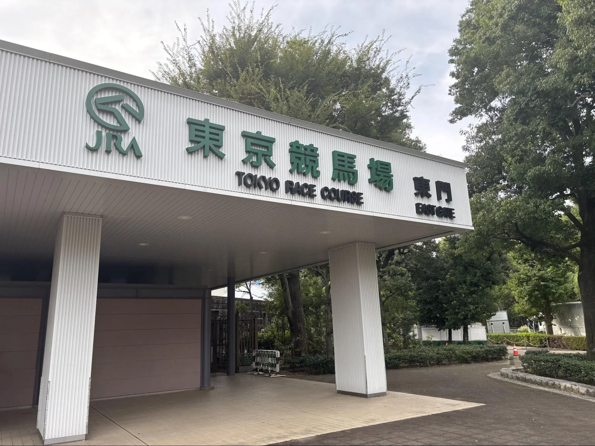 A white blocky overhang entrance surrounded by trees is the entrance to Tokyo Race Course.