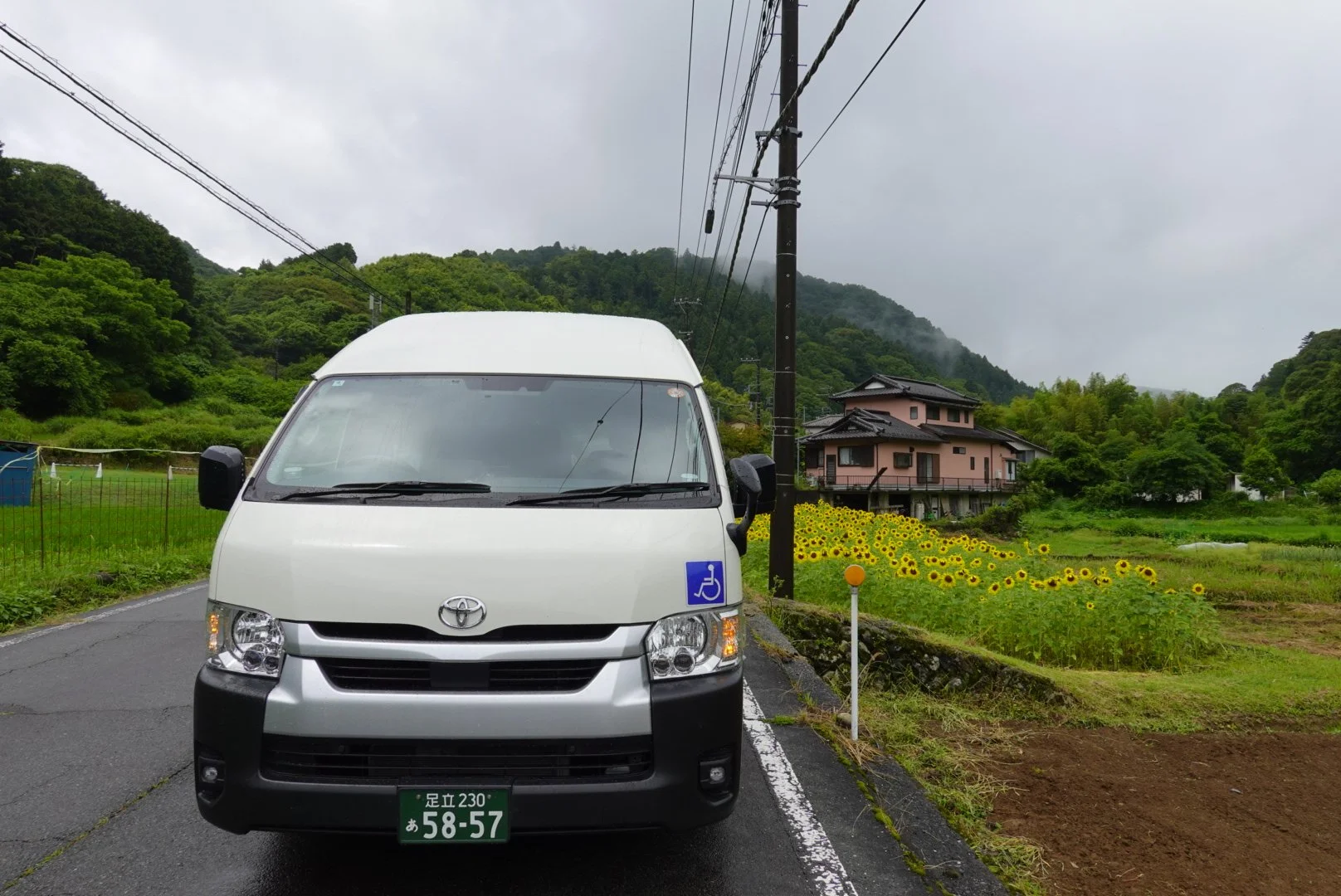 Can parked in countryside of Japan with summer flowers and an accessible sticker on the vehicle.