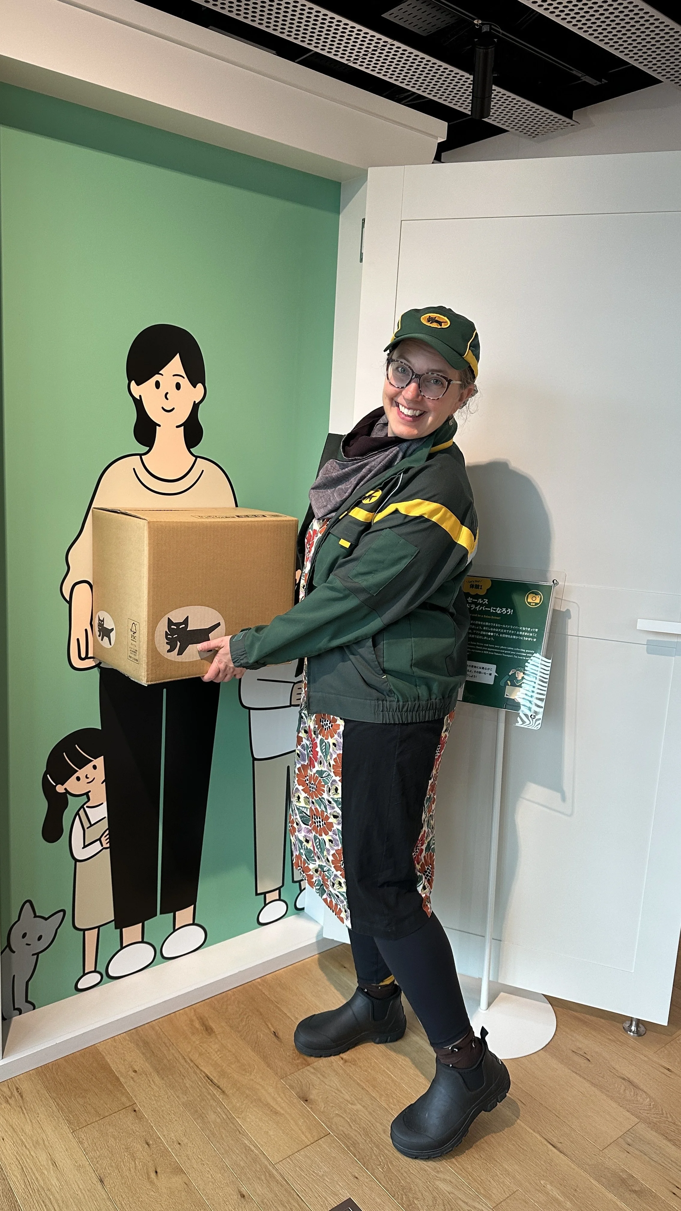 Woman wears the green and yellow uniform of Japanese logistics company Yamato and pretends to deliver a package.