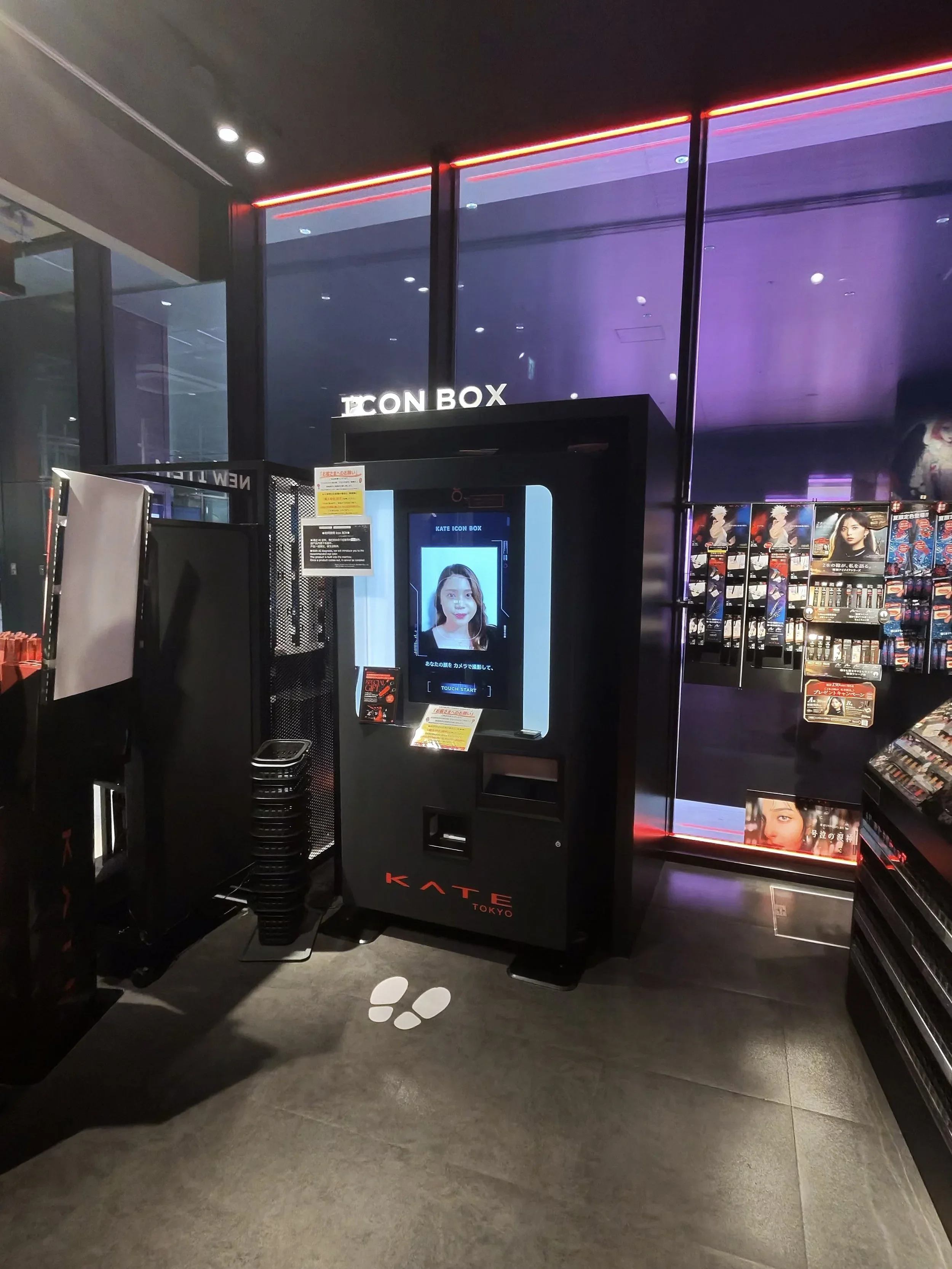 A kiosk for trying on beauty products and receiving personal advice. It is a screen mounted to a black vending machine-size box inside the corner of the KATE costmetics store.