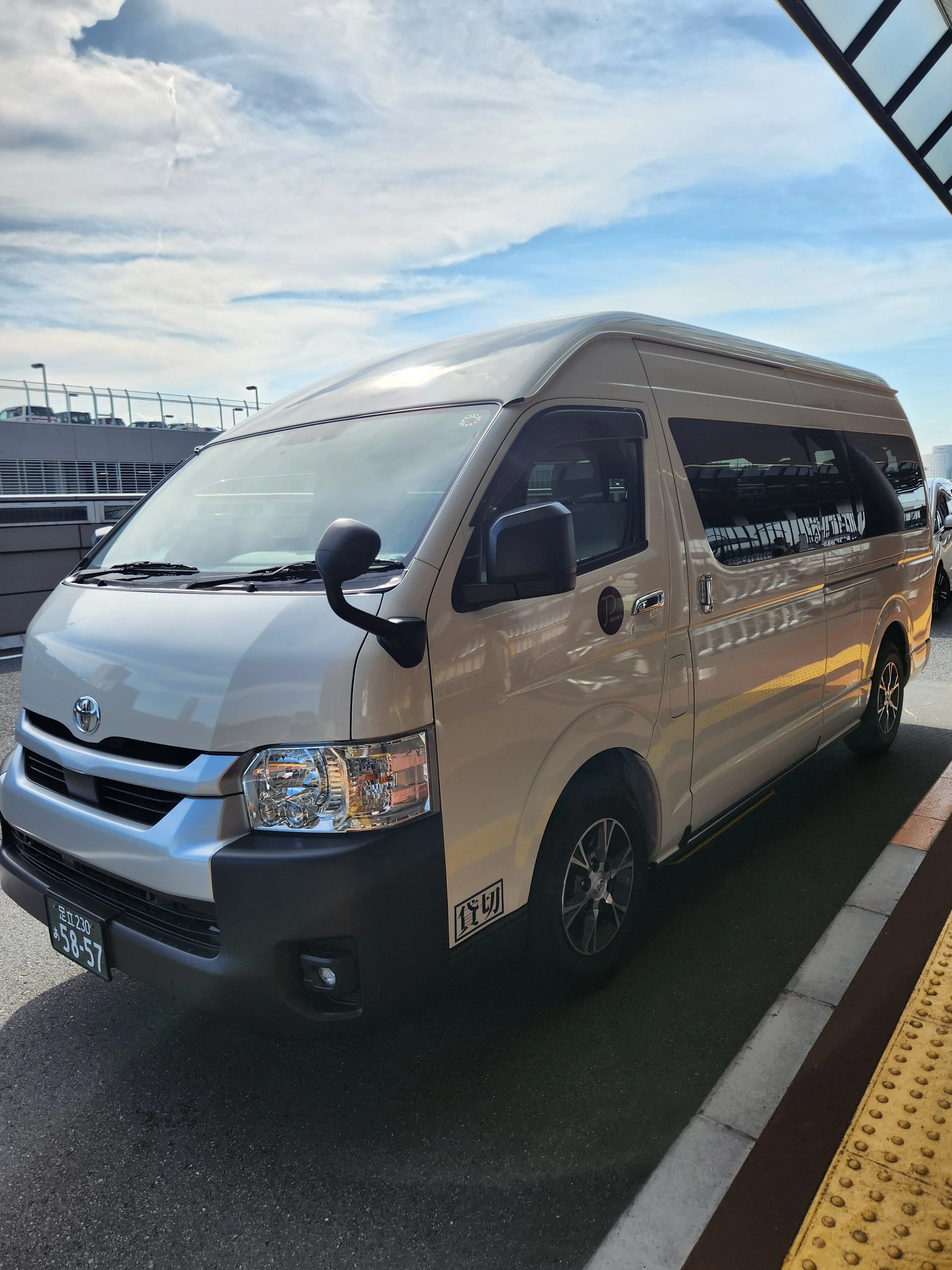 A white Toyota van parked in an outdoor parking lot with overcast sky and some buildings in the background.
