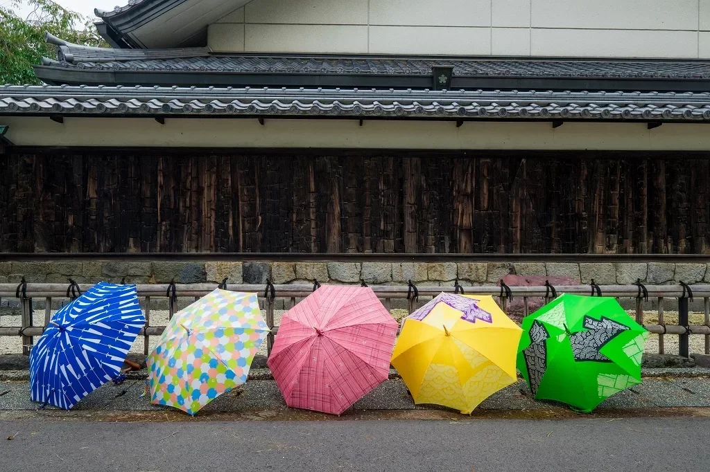 5 colorful umbrellas rest on the road in front of a traditional style Japanese building.