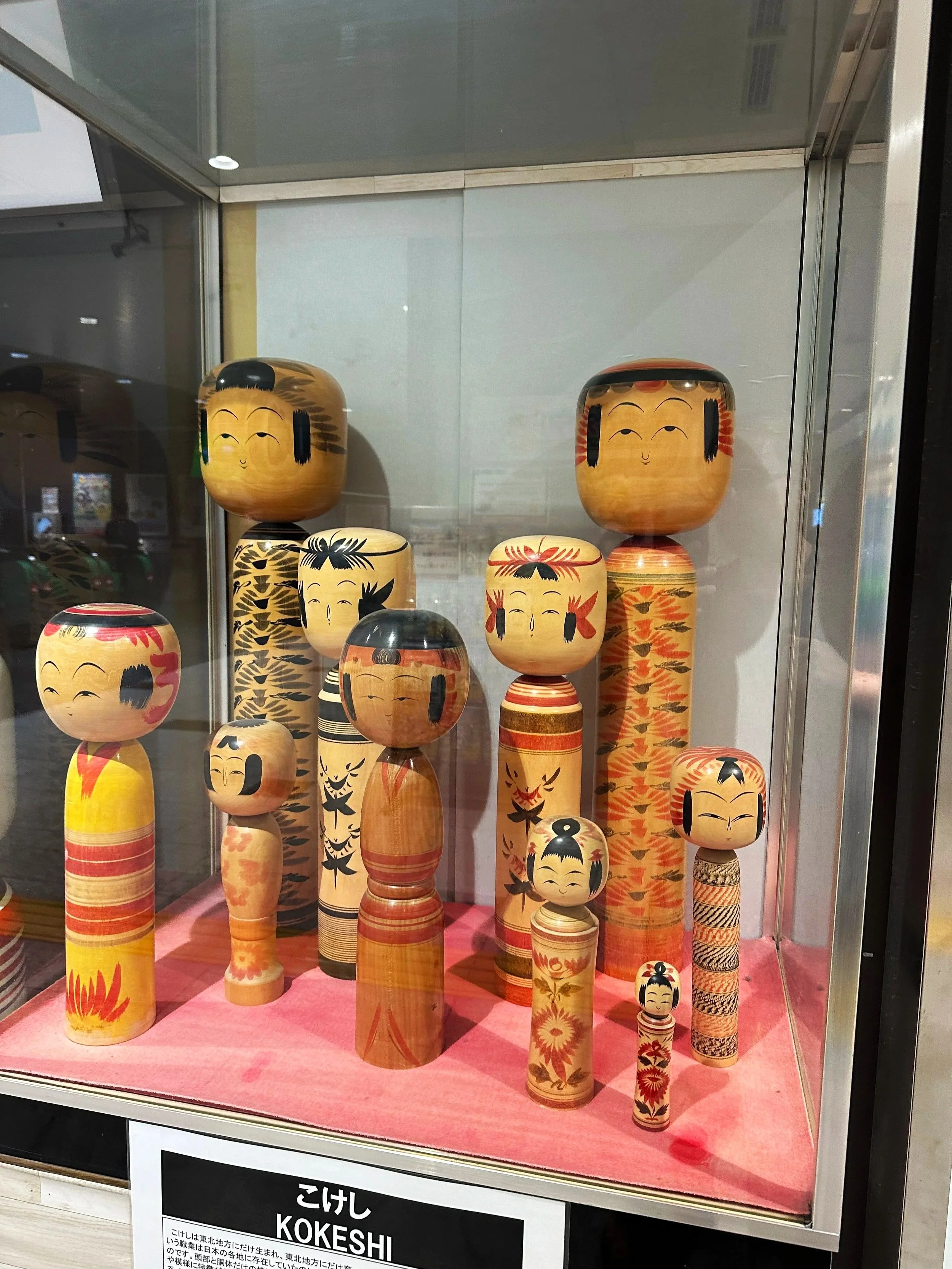 Display case of 10 different kokeshi dolls of various height and widths.