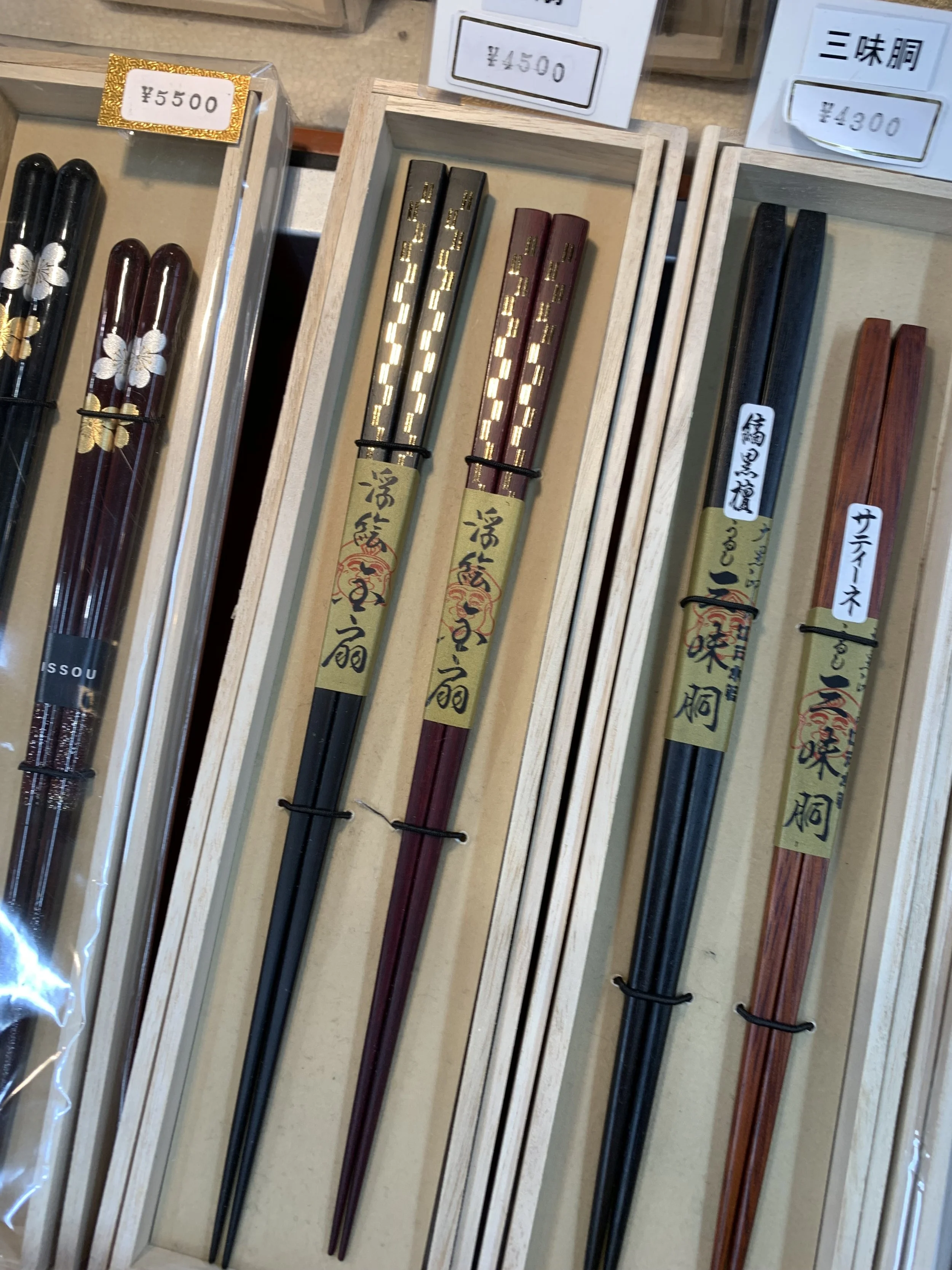 Three chopstick sets  of two with lacquer and gold lief details displayed in a wooden case.