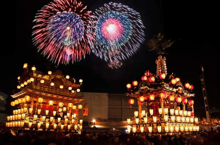 A firework festival with two firework bursts with Japanese parade floats in the foreground in Chichibu in Saitama, Japan.