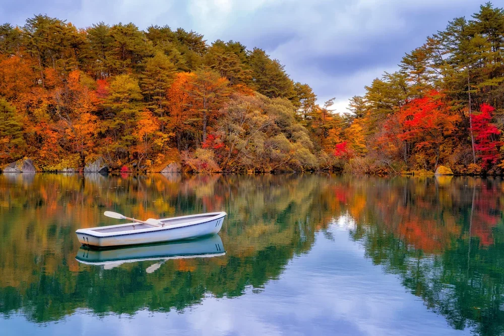 An empty rowboat sits in the middle of a lake surrounded by fall colors.