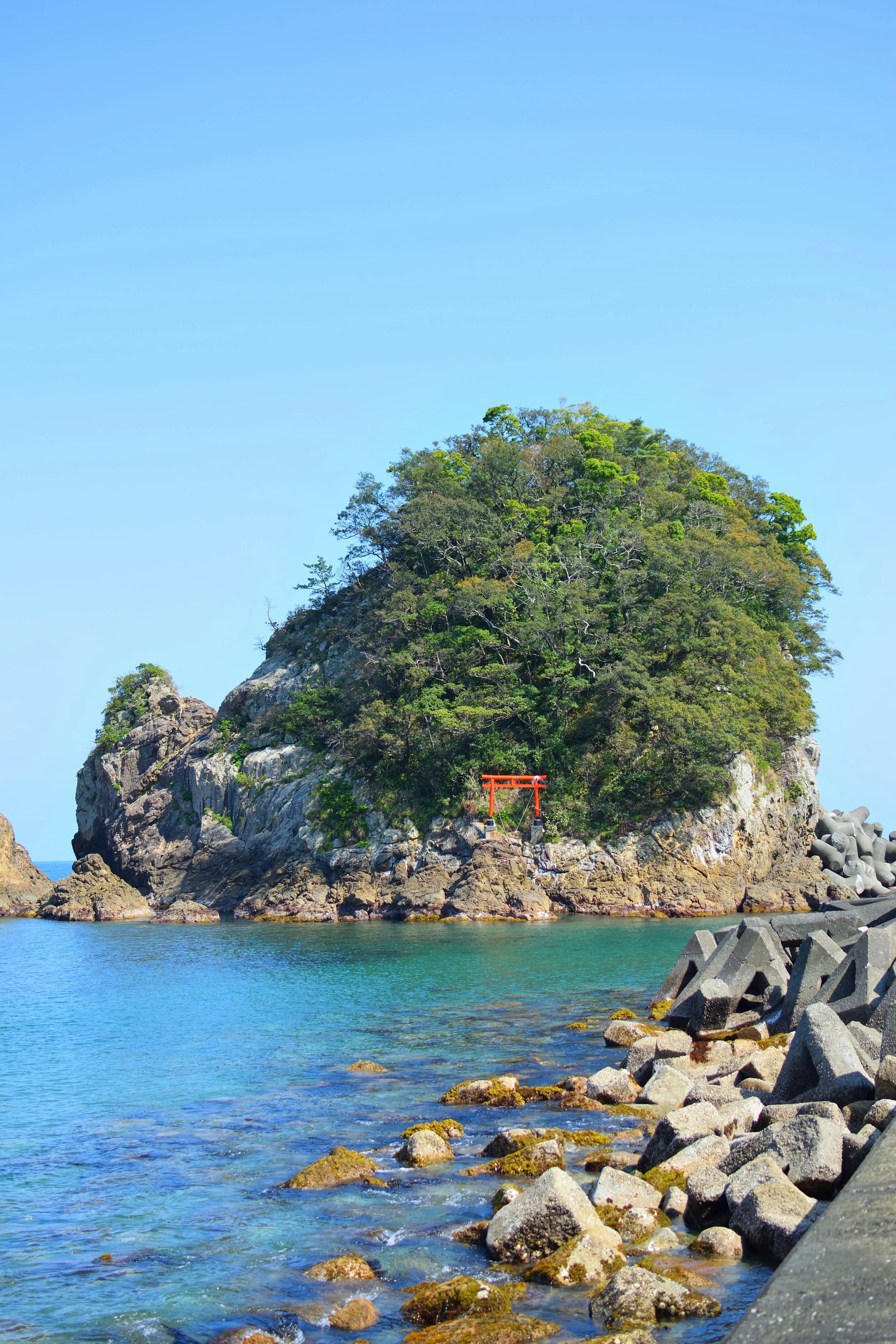 A Torii gate on an island with trees surrounded by blue green water