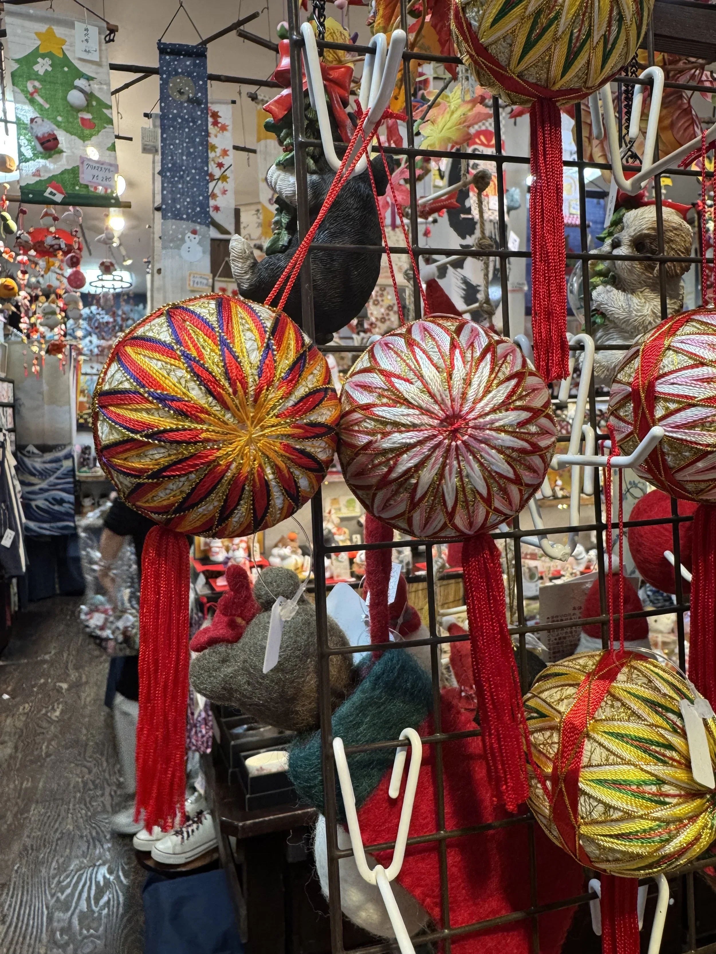 Balls covered in thread woven in intricate geometric patterns almost like snowflakes hanging by a red thread.