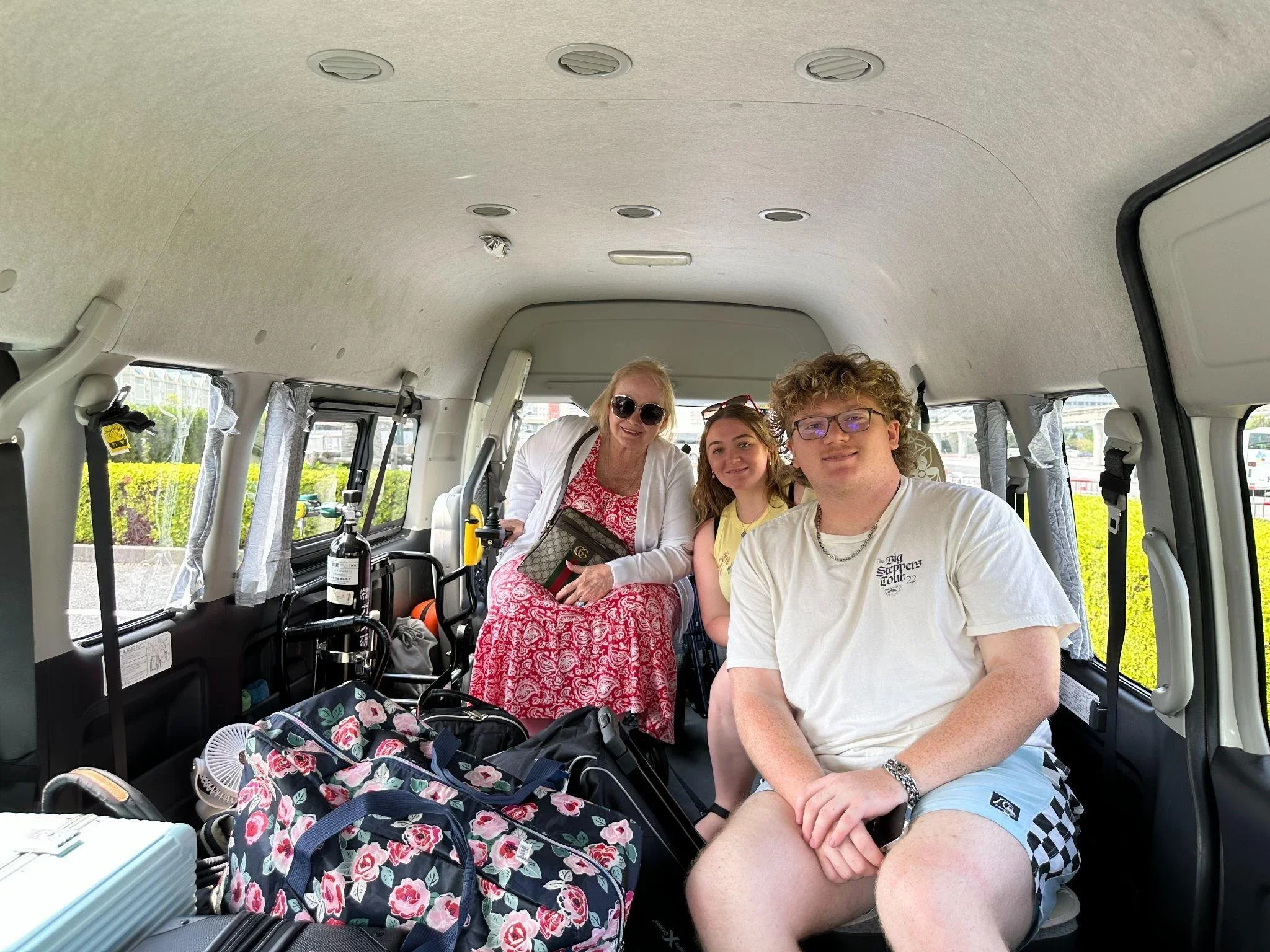 Three TokduAw guests, one male and two female, seated in the back of an accessible TokudAw vehicle smile and pose the camera.