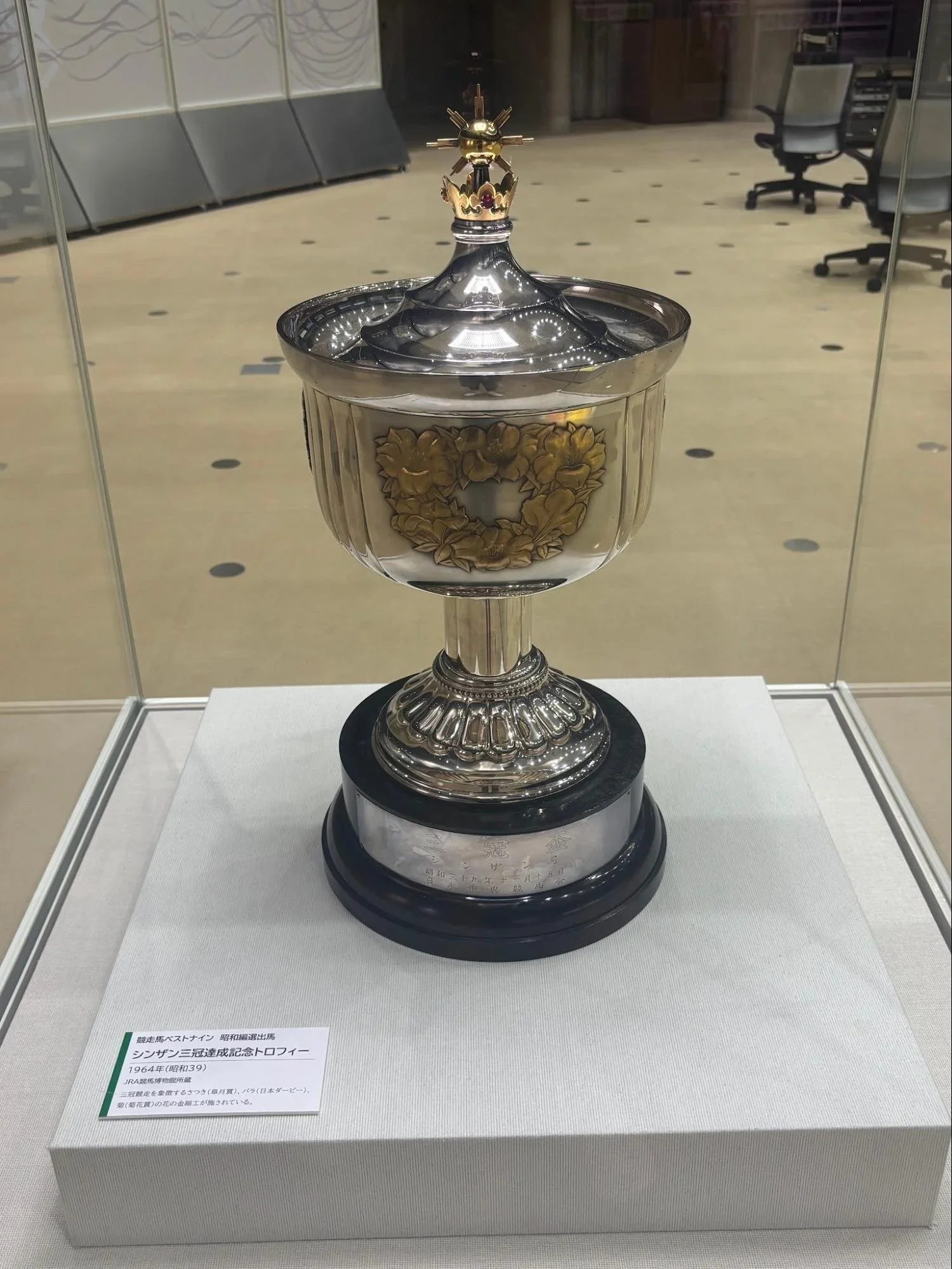 A silver and gold trophy cup sits inside a glass display case at the Tokyo Racecourse Museum.