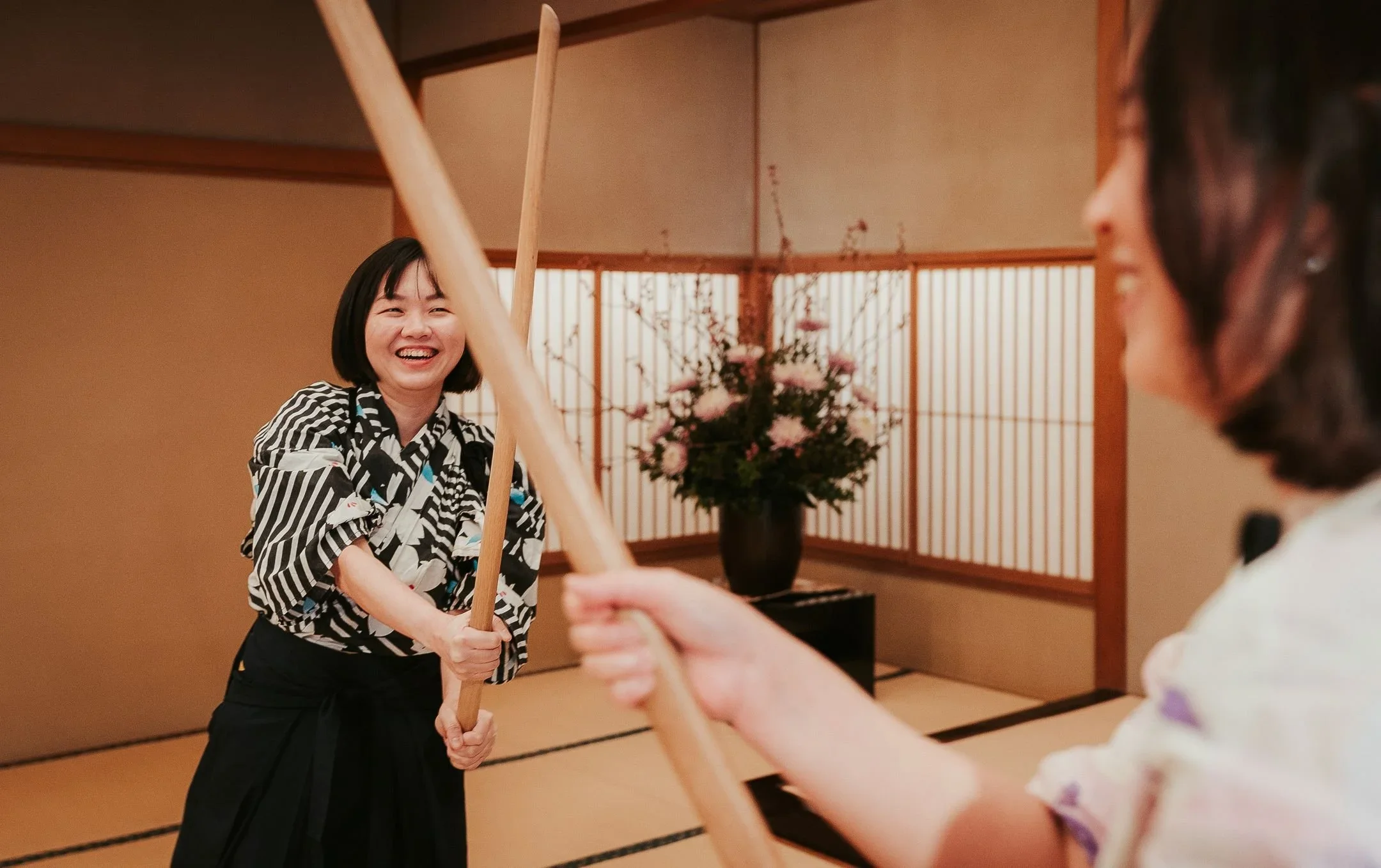Two women fight with wooden katana or Japanese swords inside a tatami mat room.