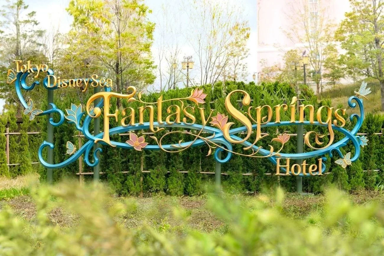 Tokyo DisneySea Fantasy Springs Hotel floral signage mounted to a fence with green bushes.