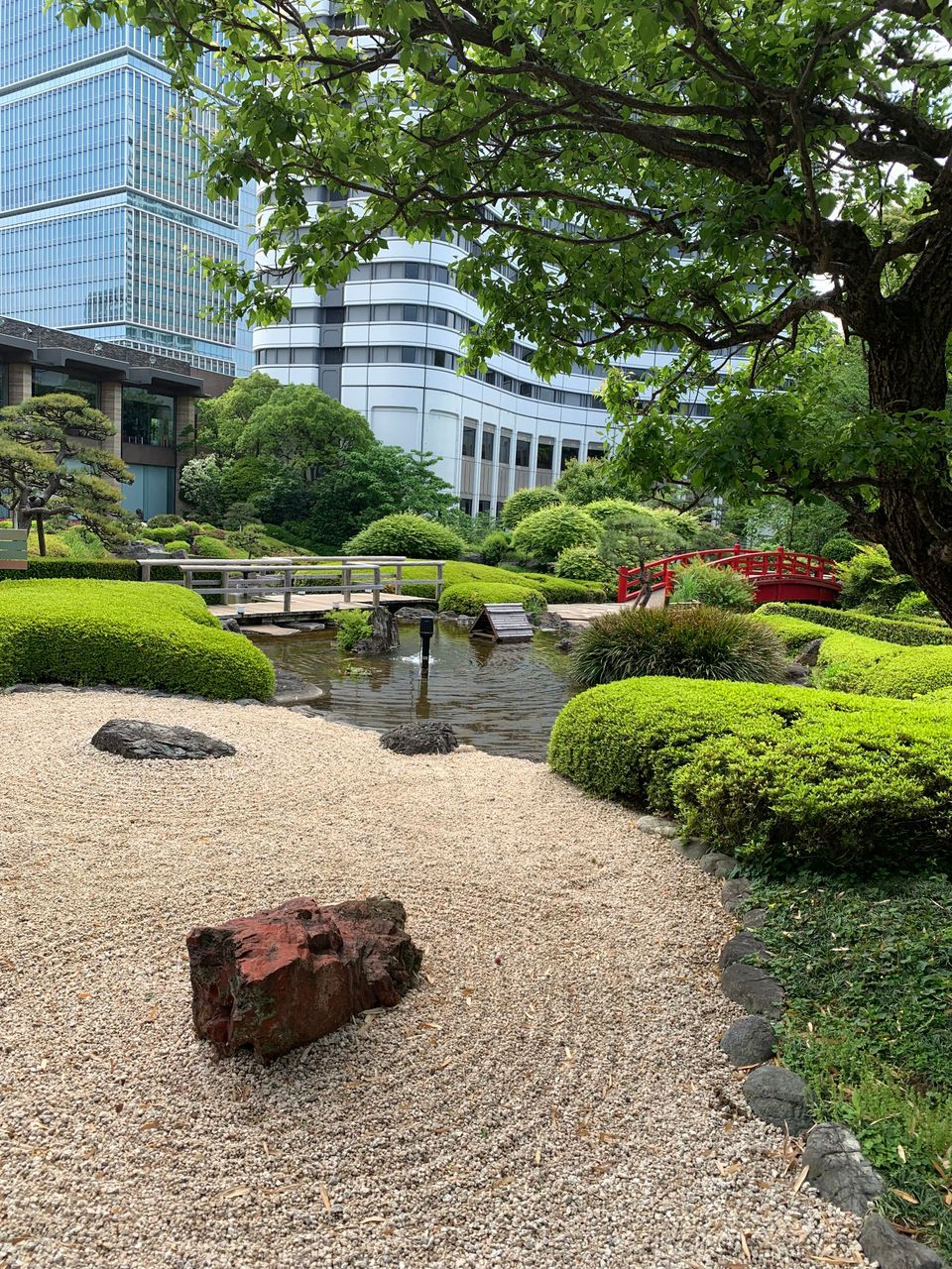 A Japanese rock garden with small pebbles forming concentric circles overlooking a pond with a red bridge.