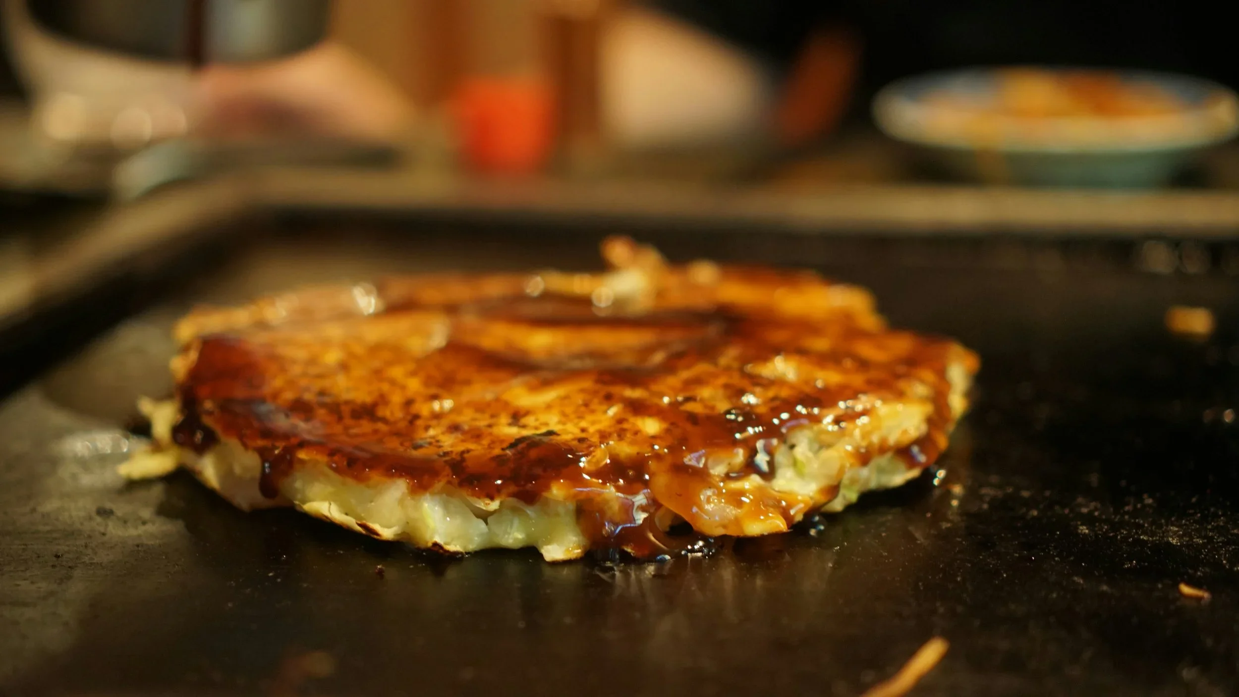 Freshly grilled okonomiyaki, a savory Japanese pancake topped with rich sauce, cooked on a teppan grill at a restaurant in Tokyo.