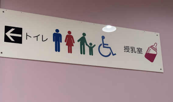 Restroom signage at the Tokyo Metro Museum featuring icons for male, female, family and accessible restrooms in addition to a nursing room mounted on a pink wall.