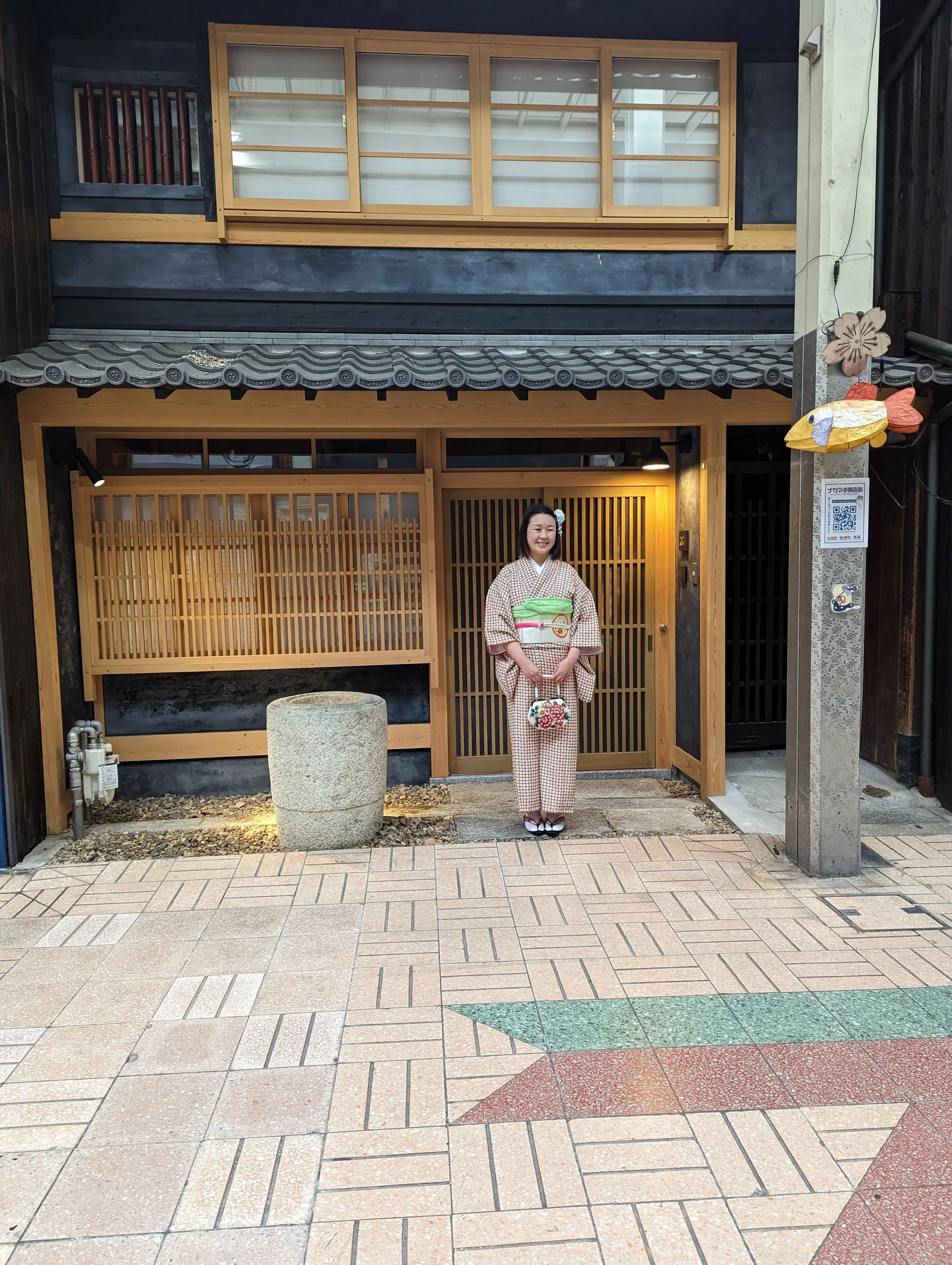 Young asian woman wearing a red and white checkered kimono with a red and white peony flower handbag standing outside of a traditional Japanese architecture building made of wood with a tiled roof.
