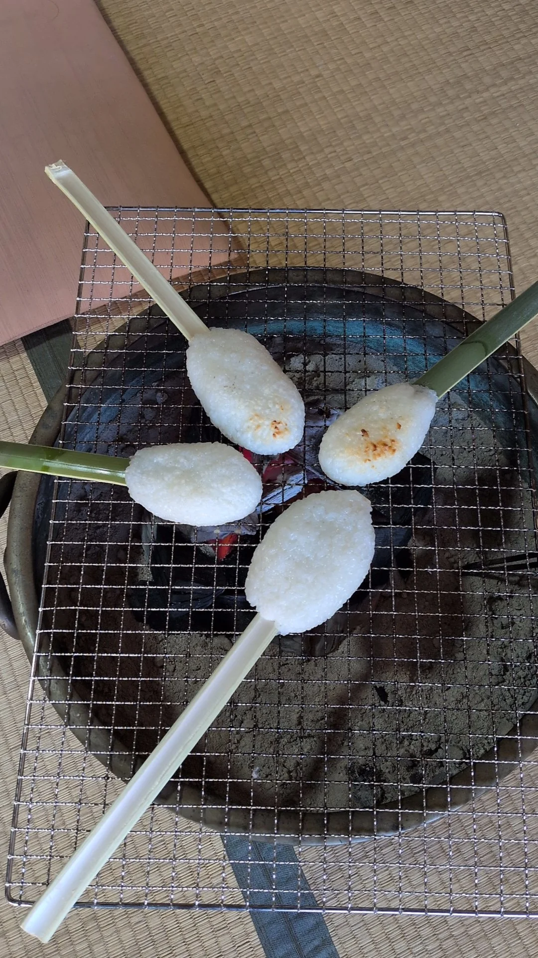 4 mochi balls on a stick being grilled, one is lightly roasted.