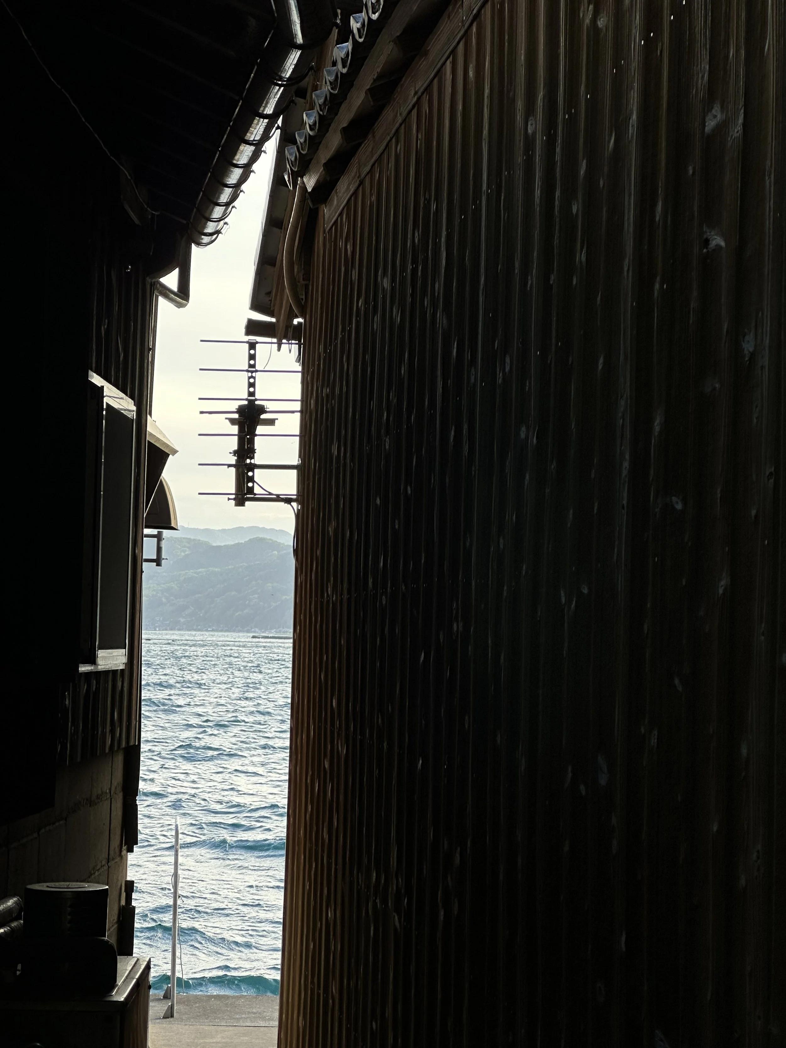 TokudAw recommendations of villages that have preserved Japanese architecture in the past including the pictured fishing buildings showing a glimpse of the Ine harbor between two buildings.