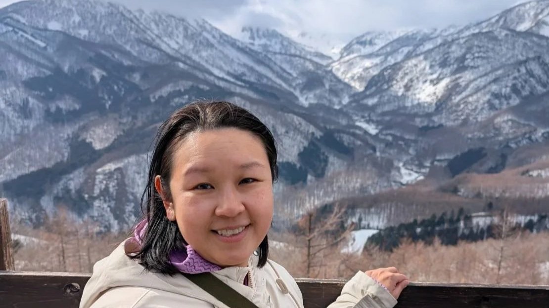 Woman on a wooden balcony with snowy mountain landscape in the background.