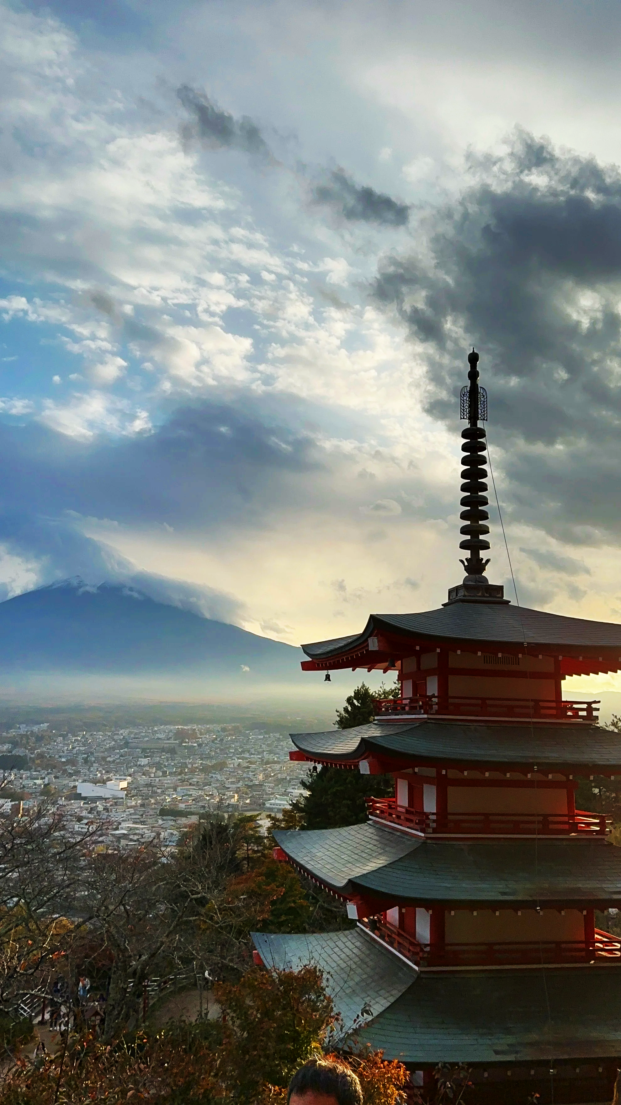 Mutli-story red pagoda at dusk with could covered Mount Fuji in the background.