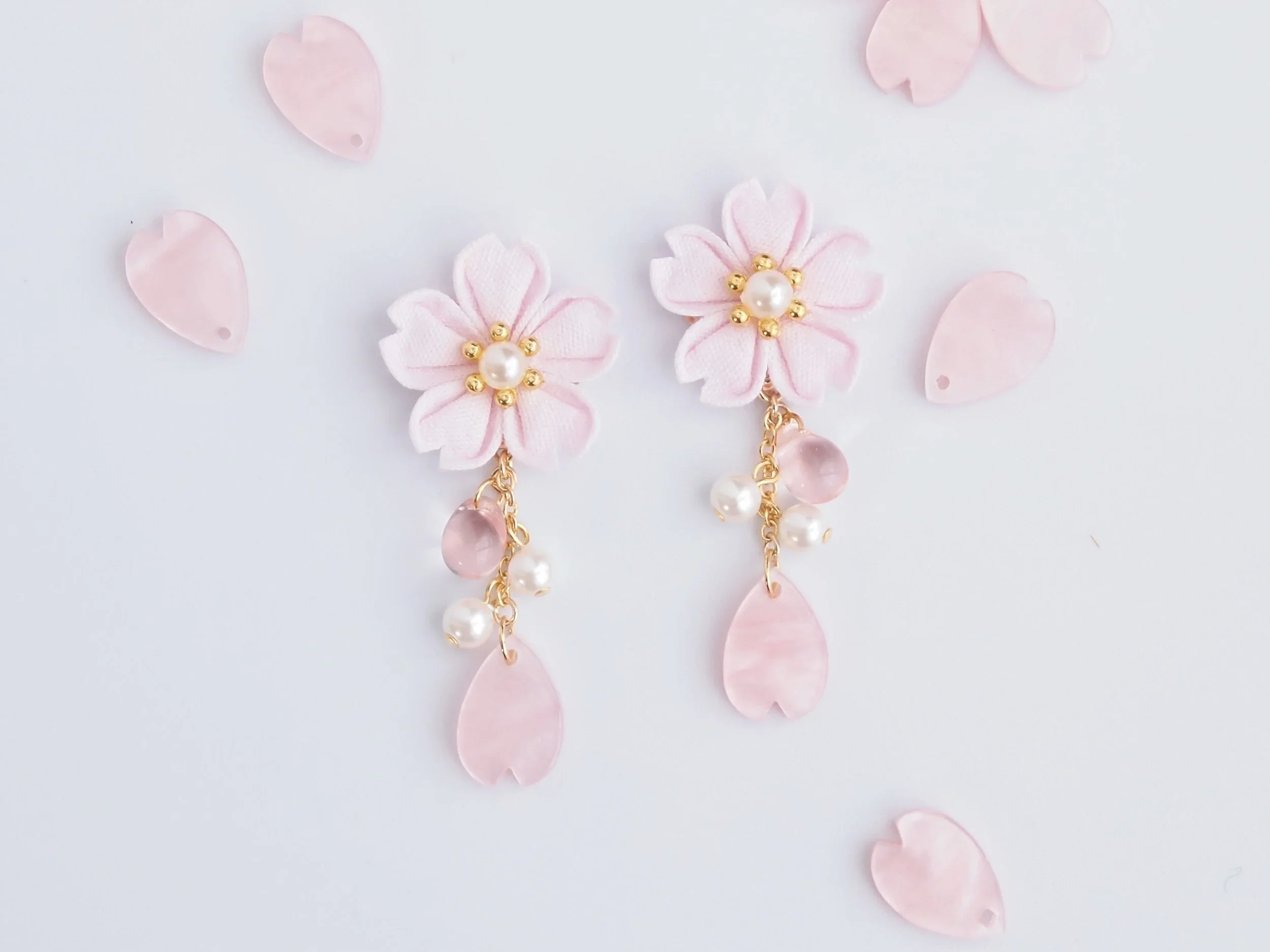 Pink cherry blossom earrings with petals in the background.