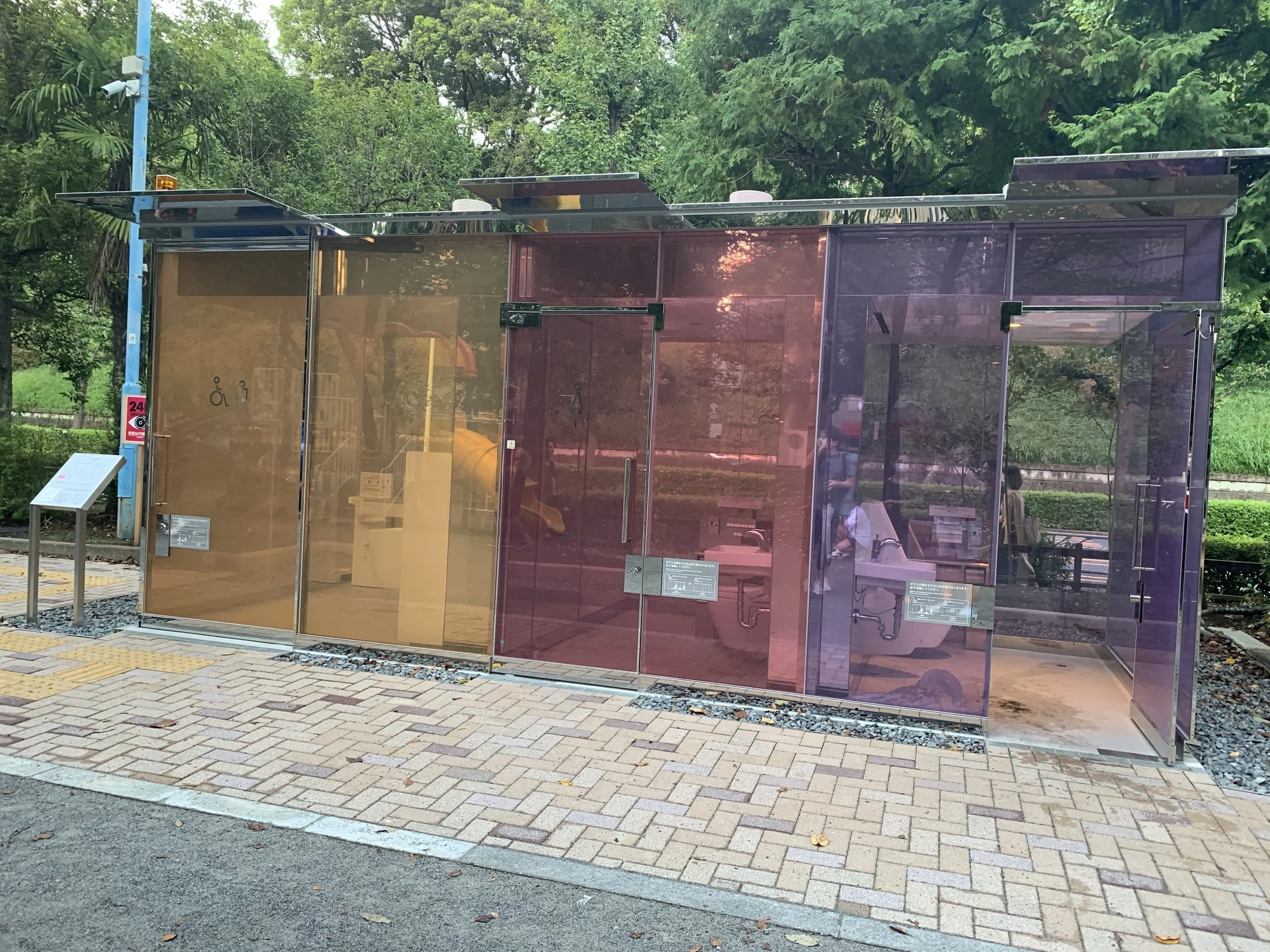 A set of 3 public toilets with transparent glass windows that turn opaque when the facility is being used.