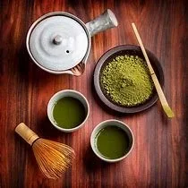 Japanese matcha in a bowl with two cups and a bamboo mixer and teapot taken from above and resting on a wooden table.