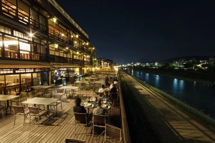 A multi-story building and outdoor dining patio along a river at night in Osaka, Japan.