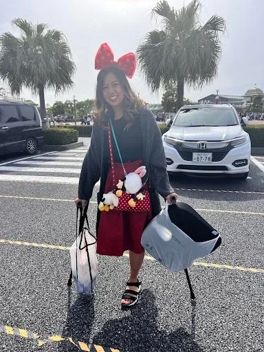 Asian woman dressed for Disney uses a cane while walking through the parking lot at Tokyo Disney.