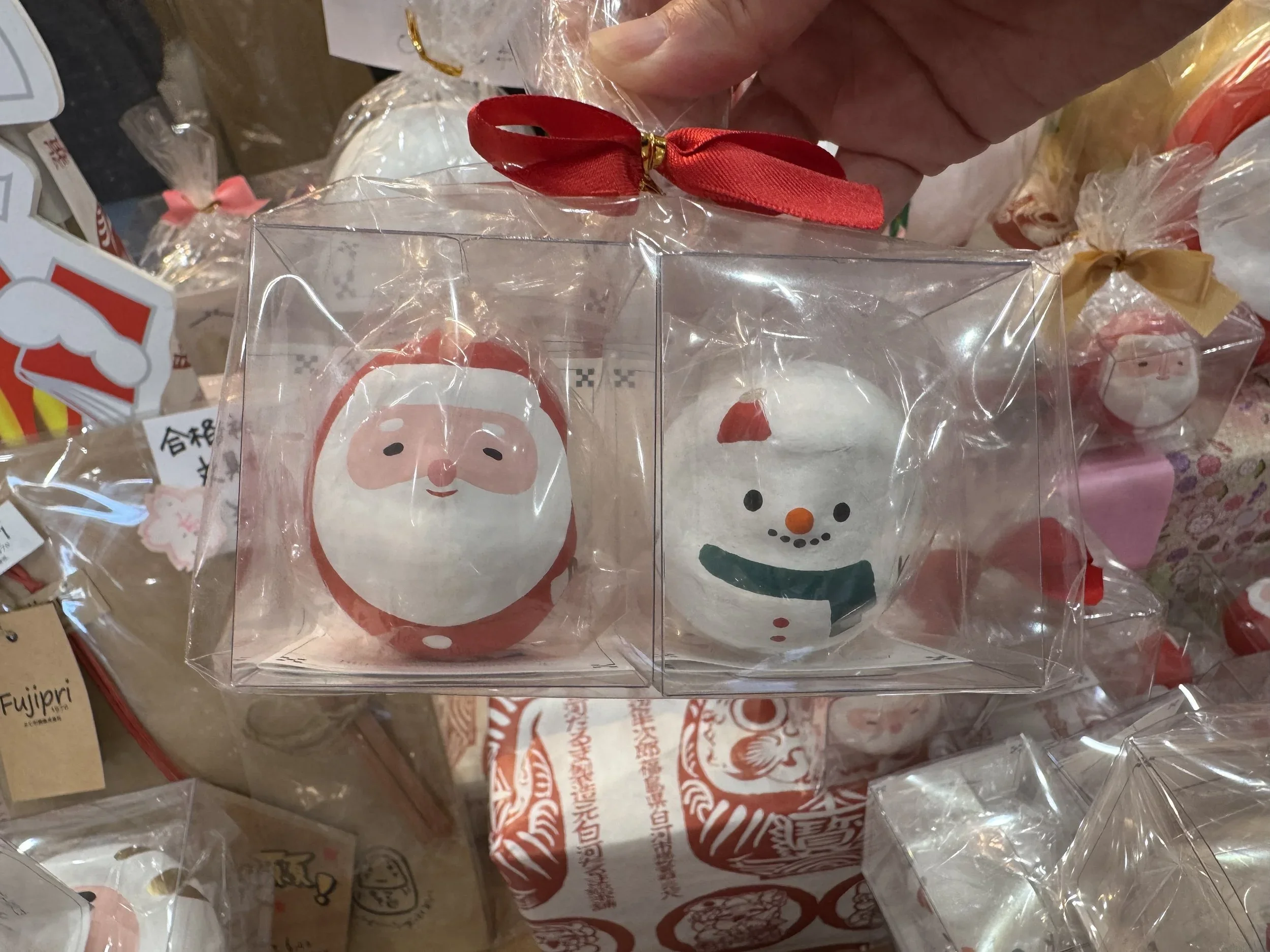 Small round Japanese Snowmen and Santa Clause daruma dolls in a clear box packaged for a Christmas gift.
