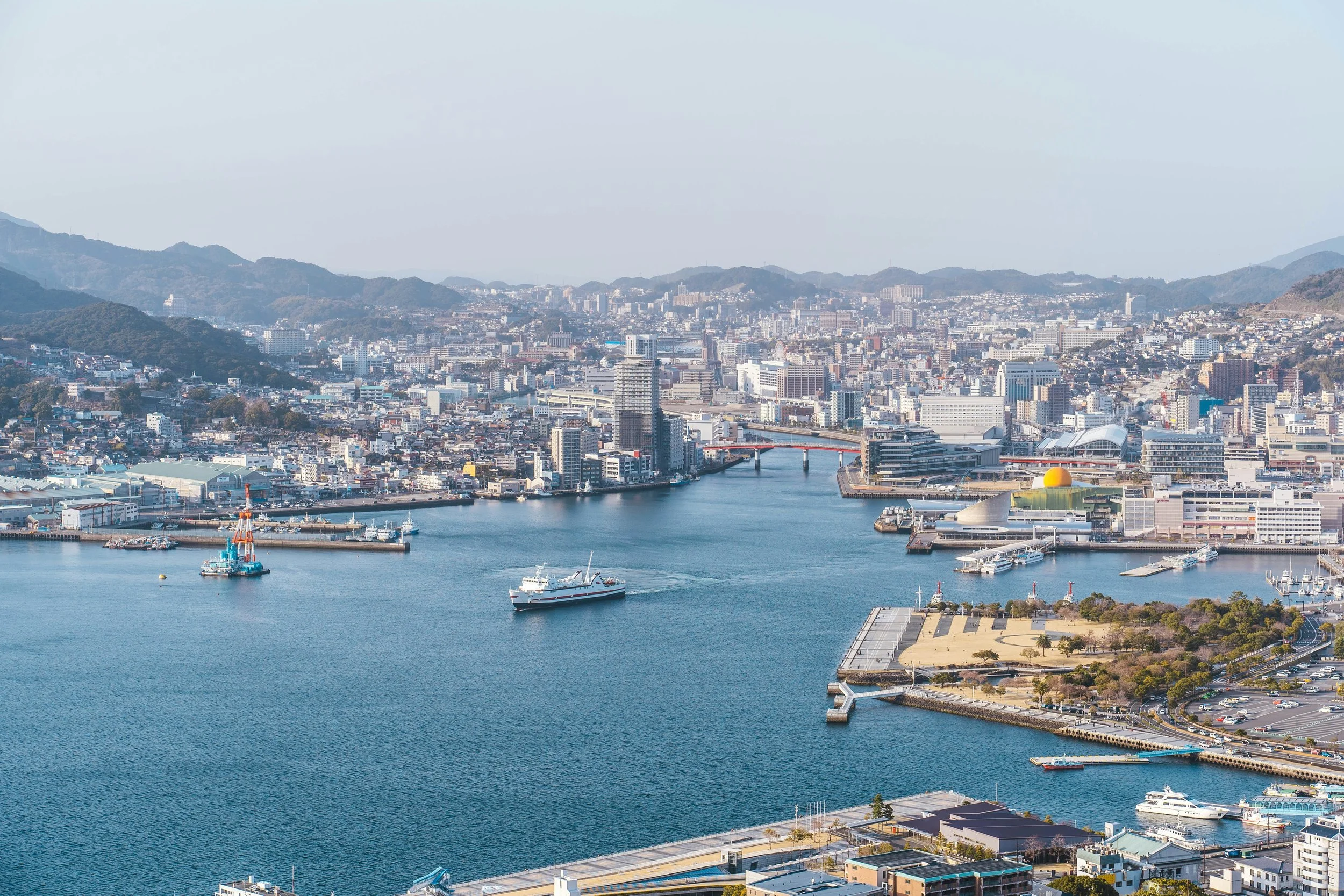 An ariel view of the bay of Nagasaki on a sunny day with a cruse ship in the water.