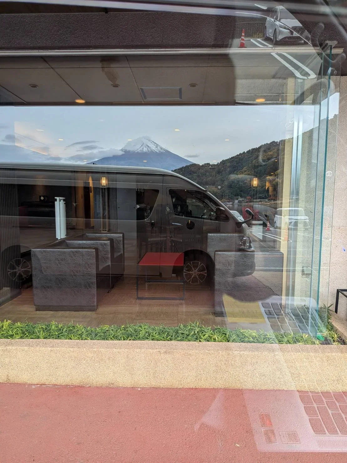 Mount Fuji and a TokudAw Japan Private Drivers Vehicle is seen in a reflection of a hotel window.