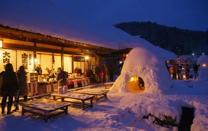 A snow lantern and hit in front of a traditional Japanese building.