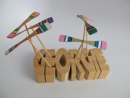 Several wooden dragonfly or propeller shaped toys on a stick stand upright in a wooden cut out that says georgie.