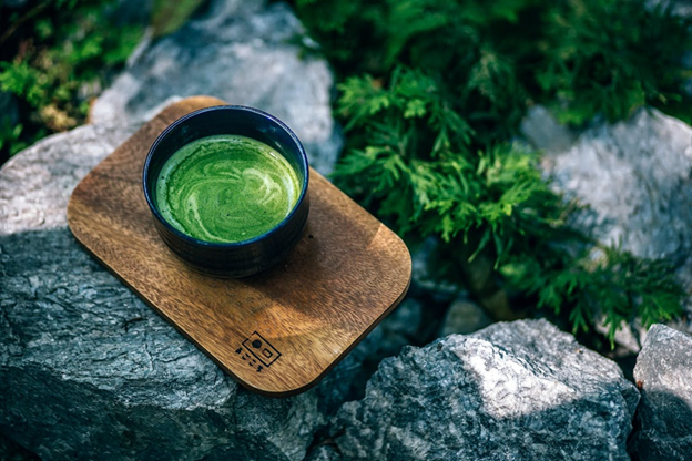 A cup of matcha rests on a wooden board on top of ricks in a rock garden.