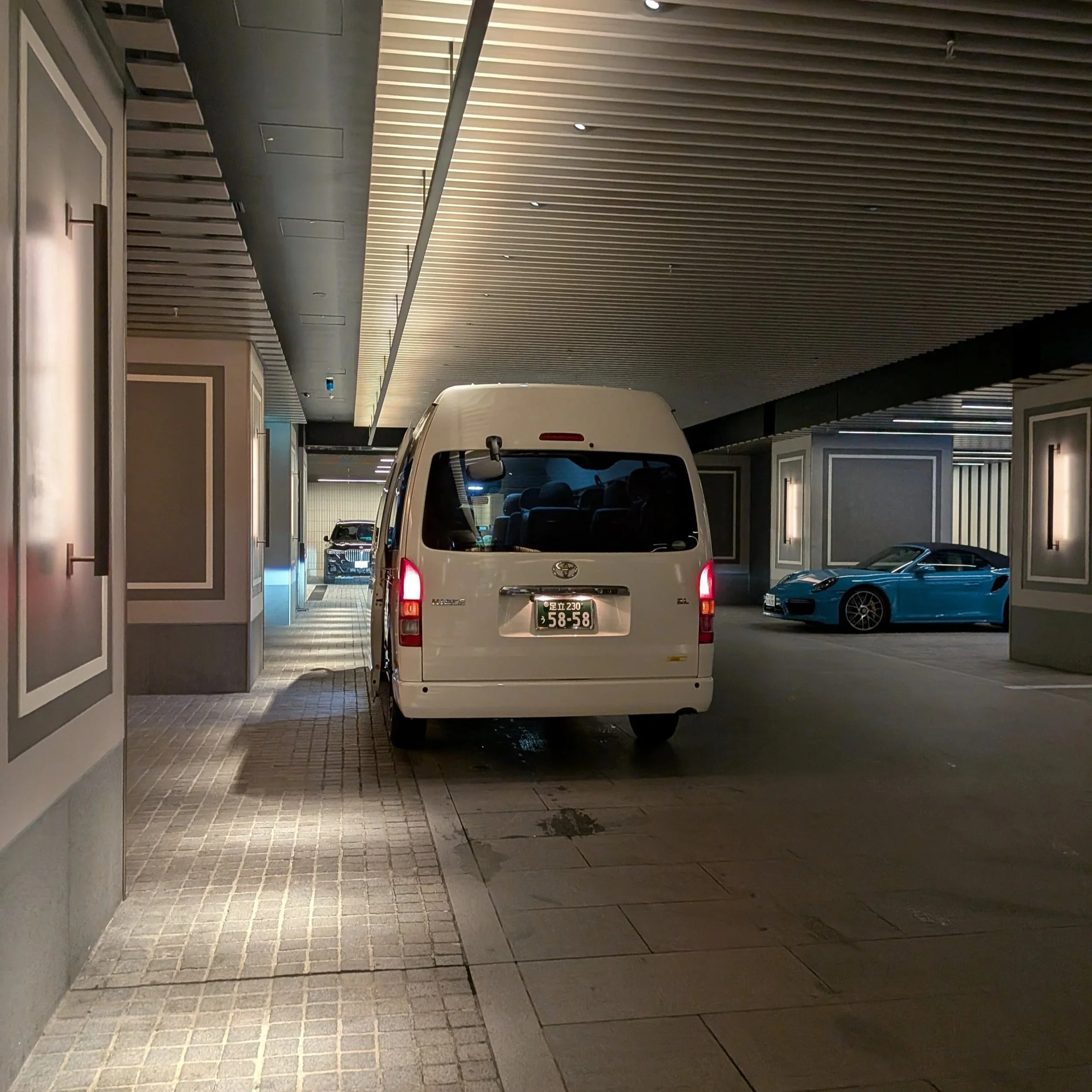 A white TokudAw vehicle waits for passengers under a covered driveway of a modern Japanese building.