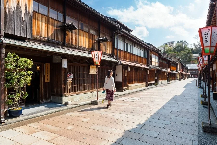 Traditional wooden Japanese chaya street in Kanazawa on a sunny cloudy day with a woman walking down the street.