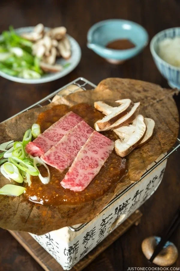Raw beef on a small stove with onions, mushrooms and a sauce nearby, a traditional dish from Gifu.