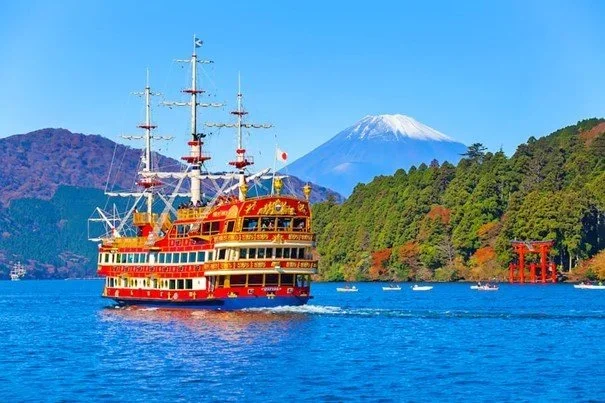 A ship-like ferry floats in a lake with Mount Fuji in the background and a red torri gate on the side.