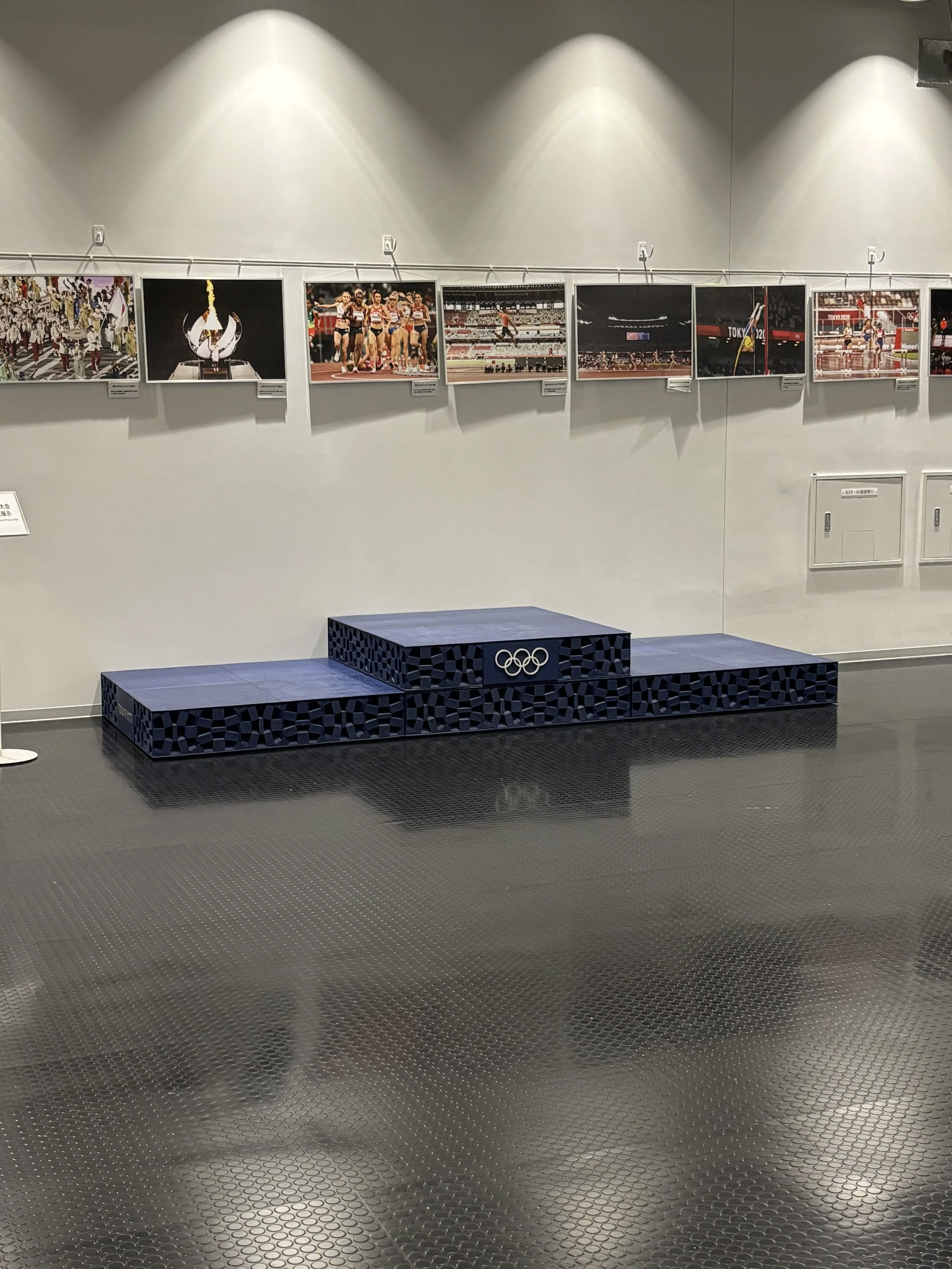 The blue Olympic podium made rests below a gallery wall of photographs from the 2020 Tokyo Olympics inside the National Stadium in Tokyo.