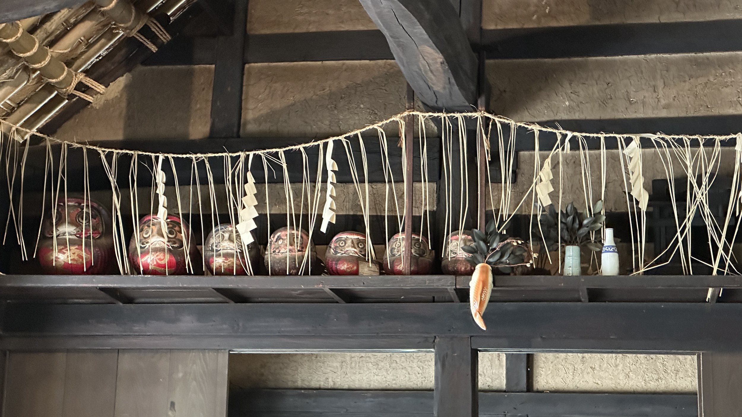 Shelf with traditional Japanese Daruma dolls, bamboo decorations, and small vases.