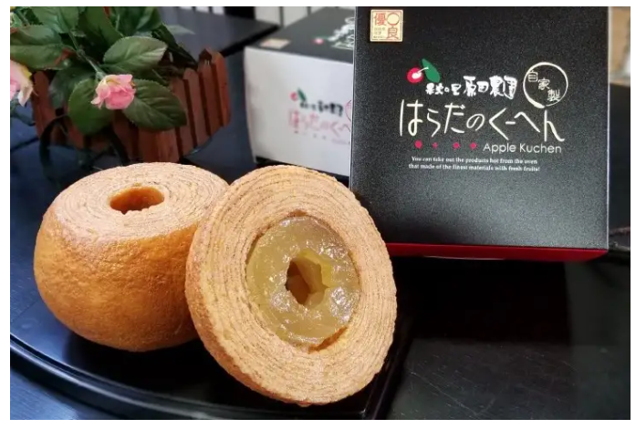 Apple ring cakes are positioned on a table in front of thier black packaging.