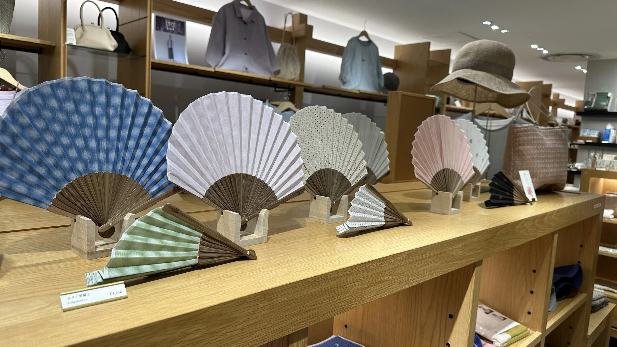 High quality Japanese fans are displayed both open and closed on top of a wooden shelf in a store