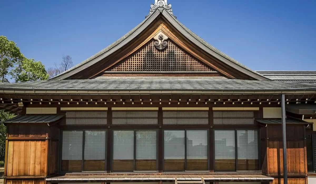 Traditional japanese building with a tiled roof and ornate tiling at roof's apex with wooden walkway on the outside of the building.
