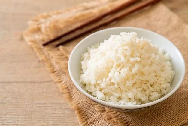 A bowl of white rice sits atop 2 burlap placemats with wooden chopsticks placed nearby.