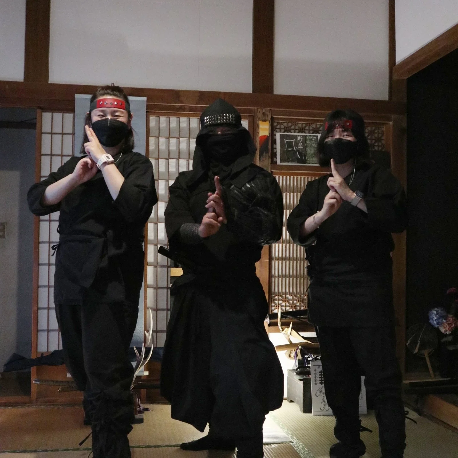Three standing people dressed in ninja outfits pose in a traditional Japanese home.