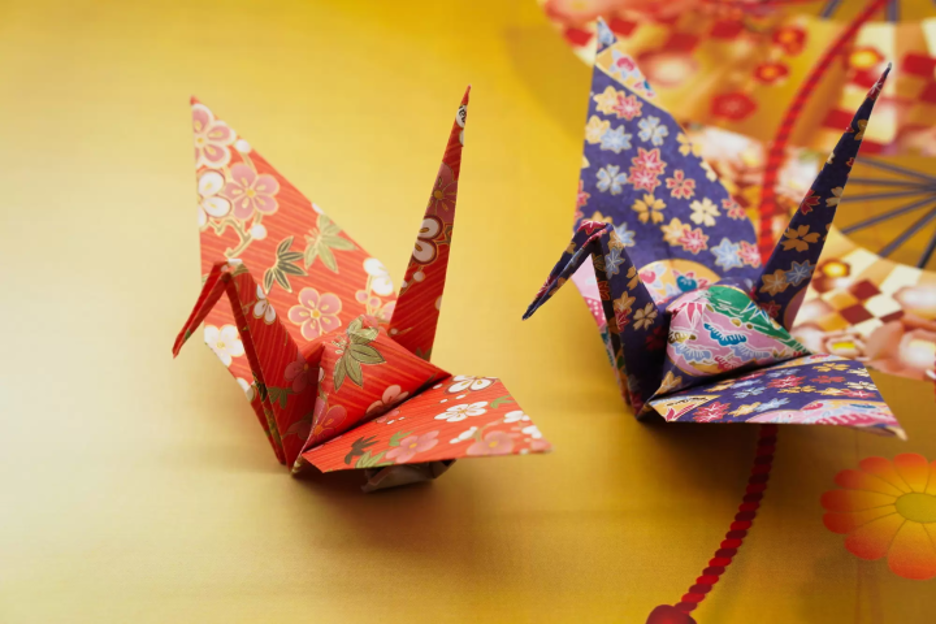 Two paper cranes made out of floral paper, one red and one purple.